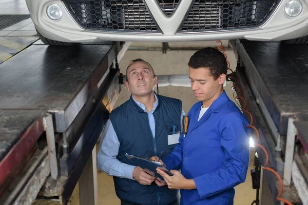 Aprendiz mecánico reparación de un coche supervisado por el mentor — Foto de Stock