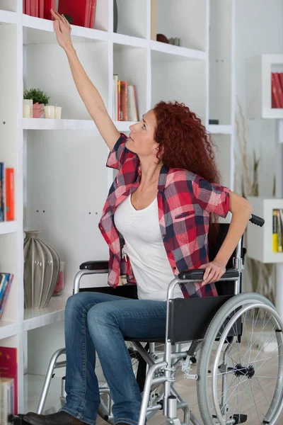 Mulher com deficiência lutando para chegar a um livro na prateleira superior — Fotografia de Stock