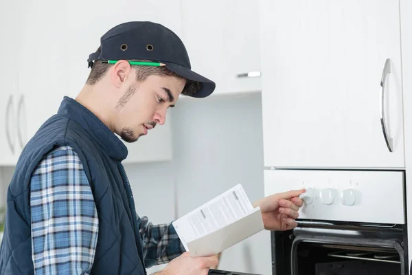 Joven reparador en general la instalación de horno nuevo en la cocina — Foto de Stock