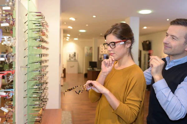 Augenärztin und schöne brünette Frau wählen Brille im Optikgeschäft — Stockfoto