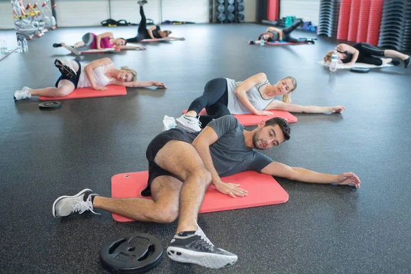 Hombres y mujeres jóvenes estirándose en el gimnasio — Foto de Stock