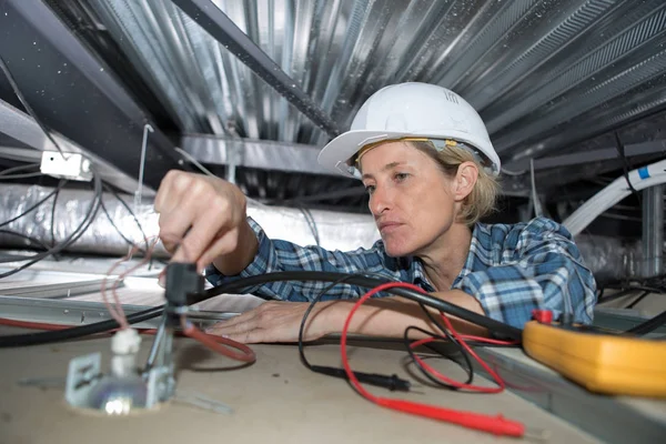 Mujer constructora fijación de electricidad en el techo — Foto de Stock