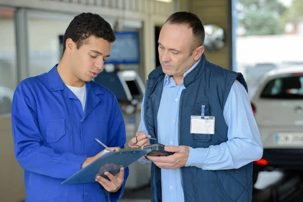 Mechanic with clipboard talking to man — Stock Photo, Image