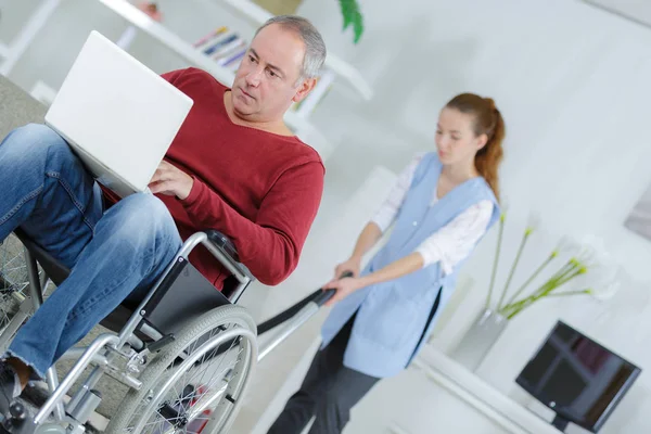 Gehandicapte man kijken film op laptop terwijl reiniger werkt — Stockfoto