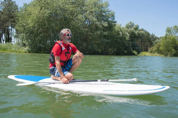 Maduro atractivo jinete contemplando la naturaleza sentado en paddle board —  Fotos de Stock