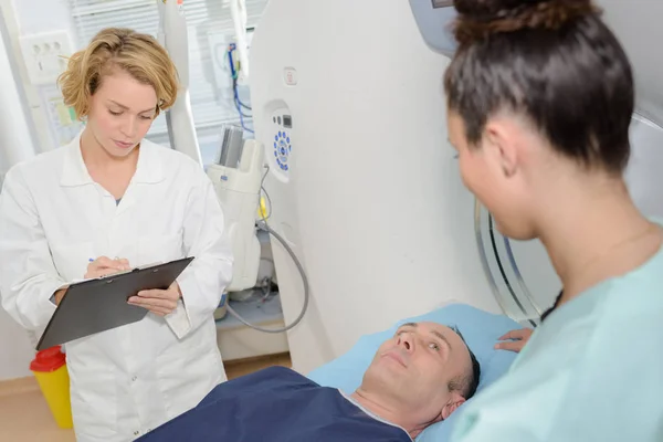 Médecin remplissant le formulaire, patient couché sur le lit — Photo