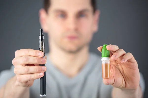 Homem mostrando um cigarro eletrônico ajustável e seu líquido — Fotografia de Stock