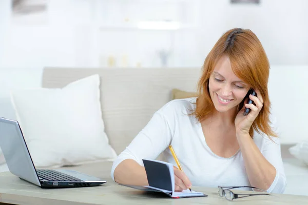 Kvinna med mobiltelefon skriva ner utnämning i hennes dagbok — Stockfoto