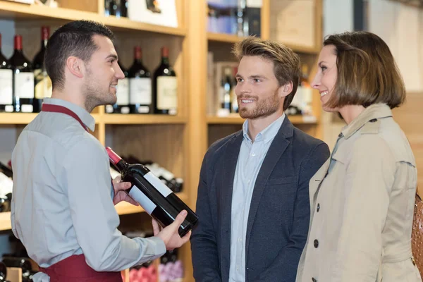 Commerçant recommandant du vin au jeune couple — Photo