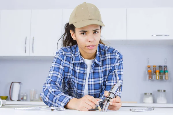 Jovem mulher fixação pia em clientes cozinha — Fotografia de Stock