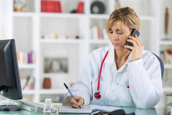 Médico femenino de mediana edad al teléfono en el consultorio —  Fotos de Stock