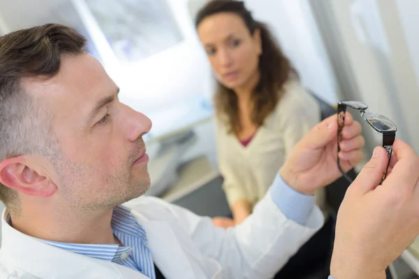 Optician checking glasses of a woman at optics store — Stock Photo, Image