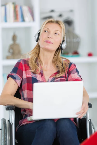 Mulher em cadeira de rodas usando laptop enquanto ouve música — Fotografia de Stock