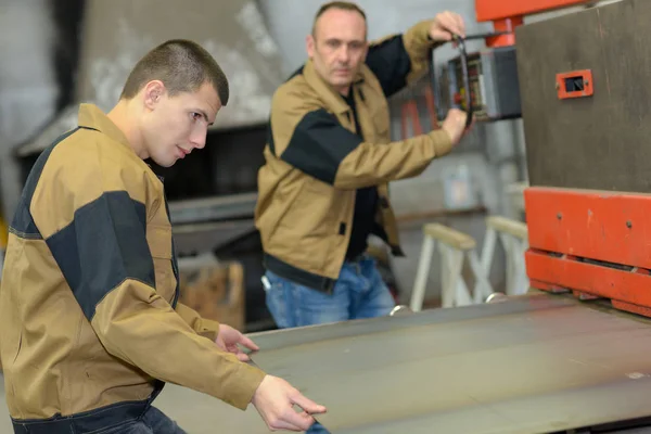 Engineer cutting sheet metal with apprentice — Stock Photo, Image