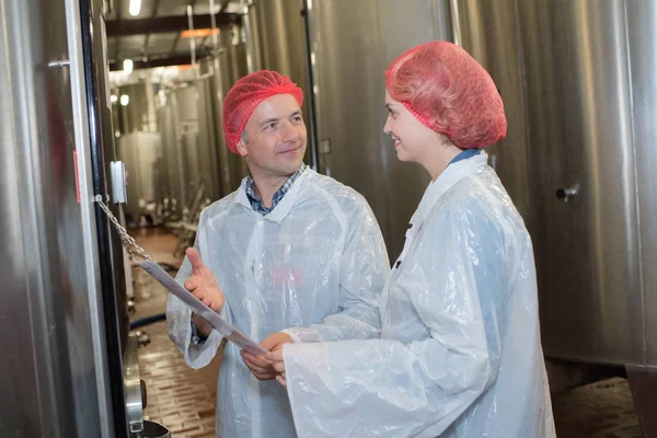 Científico hablando con su colega sujetando portapapeles en la fábrica —  Fotos de Stock