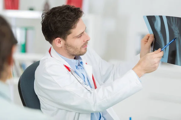 Doctor masculino con paciente mirando rayos X en el consultorio —  Fotos de Stock