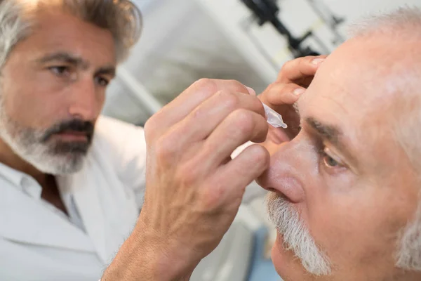 Arzt träufelt Augentropfen auf Seniorin — Stockfoto