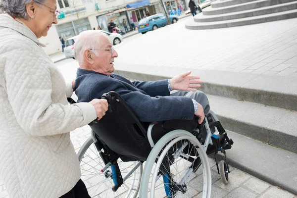 Pareja de ancianos que tienen problemas para mover marido discapacitado a través de la ciudad —  Fotos de Stock