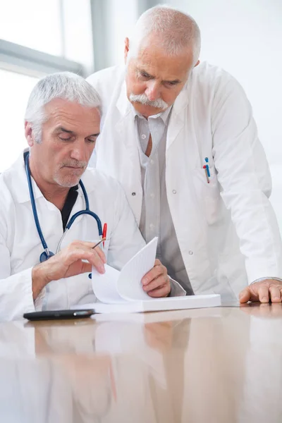 Старші лікарі чоловічої статі за столом перевіряють документи — стокове фото