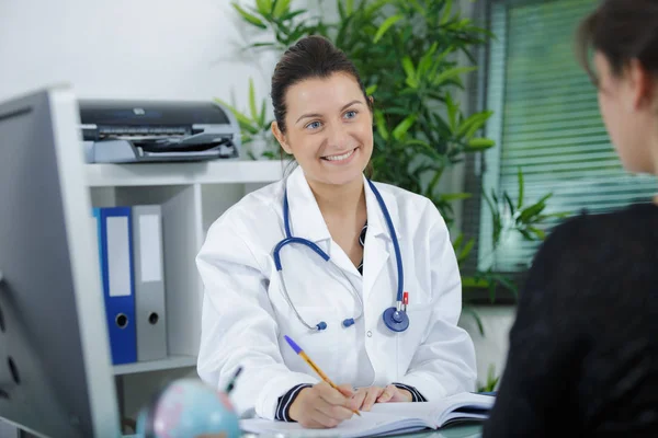 Hermosa doctora sonriendo a paciente en el consultorio —  Fotos de Stock