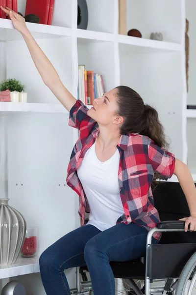 Mujer en silla de ruedas tratando de llegar a un estante — Foto de Stock