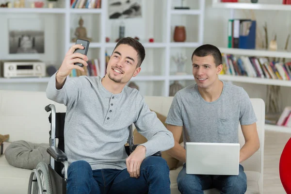 Jeune homme en fauteuil roulant parler un selfie avec un ami — Photo