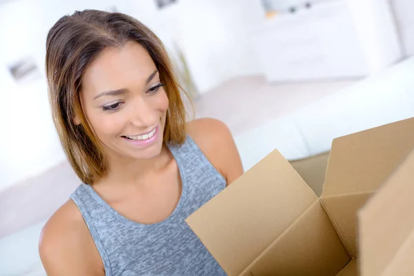 Sonrisa dentada mujer abriendo paquete en casa — Foto de Stock