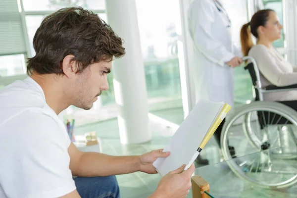Молодий чоловік читає під час очікування в лікарні лобб — стокове фото