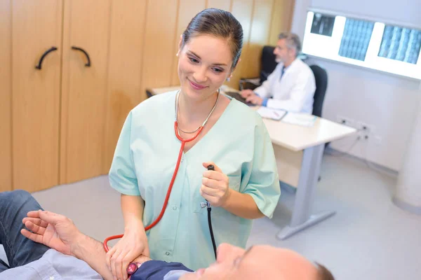 Медсестра заспокійливо посміхається пацієнту під час перевірки артеріального тиску — стокове фото