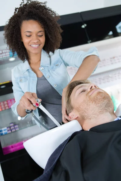 Косметолог моет волосы клиентам мужского пола в салоне — стоковое фото