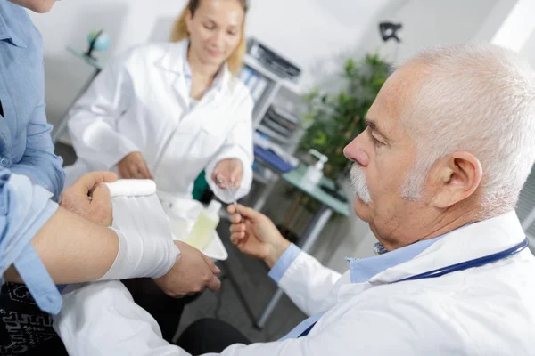 Médico sênior enfaixando sua mão paciente em consultório médico — Fotografia de Stock