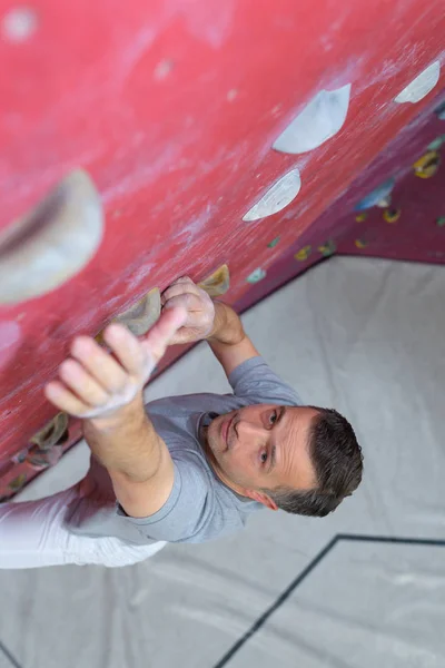 man climber on artificial climbing wall in bouldering gym