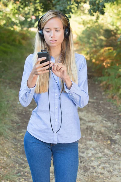 Mujer joven escuchando música en un teléfono inteligente al aire libre —  Fotos de Stock