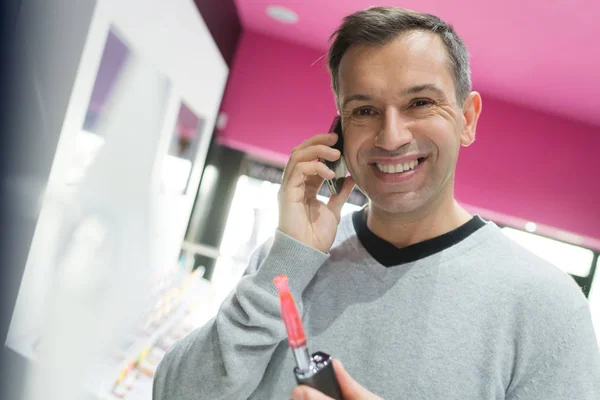 Man met behulp van een telefoon tijdens kiest een vapourizer — Stockfoto