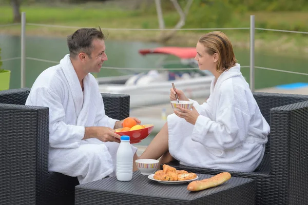 Pareja sentada al aire libre desayunando usando albornoces — Foto de Stock