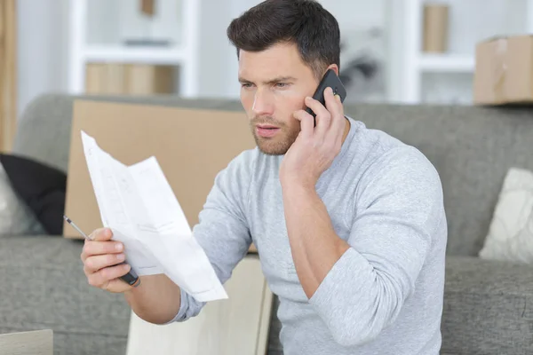 Hombre usando el teléfono mientras monta estante en casa —  Fotos de Stock