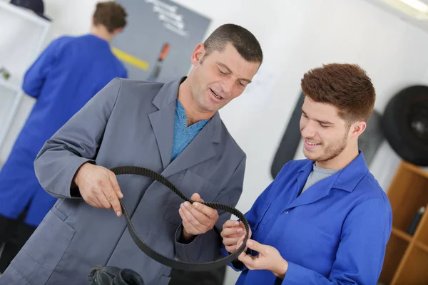 Trainee nechanic med instruktör innehav gummi bälte — Stockfoto