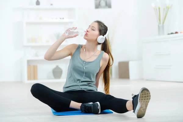 Giovane donna sta bevendo acqua dopo l'allenamento su tappetino sportivo — Foto Stock