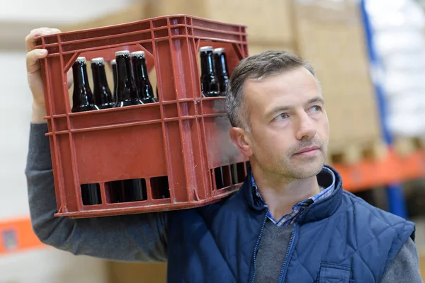 Retrato de homem segurando garrafas de cerveja em caixa na cervejaria — Fotografia de Stock