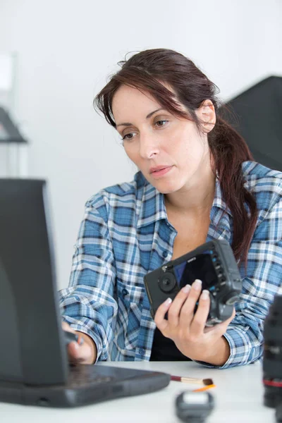 Bir kamera tutarak ve laptop içine yazarak kadın — Stok fotoğraf