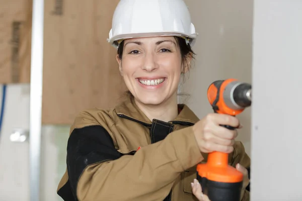 Gärna kvinnliga builder i hjälm med borr i händer leende — Stockfoto