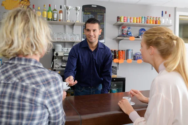 Alegre barista hablando con mujeres jóvenes en la cafetería —  Fotos de Stock