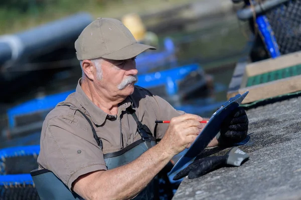 Viejo piscicultor contando stocks en portapapeles — Foto de Stock