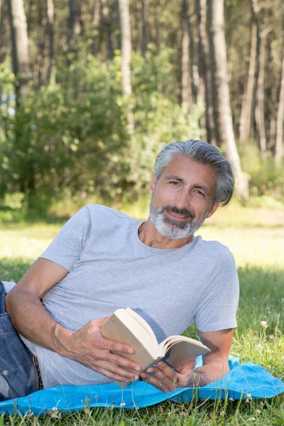 Adam lyingsitting bir kitap okuma çim — Stok fotoğraf