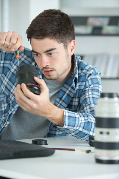 Ориентированный молодой человек чинит ретро-камеру на своем рабочем месте — стоковое фото