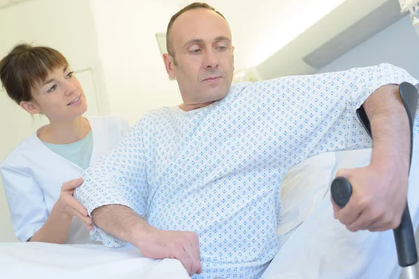 Paciente amarrando para sair da cama do hospital com muletas — Fotografia de Stock