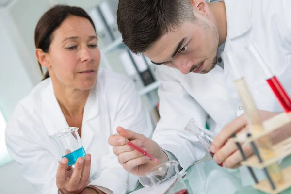 Joven químico sonriendo mientras sostiene la pipeta de prueba en el laboratorio — Foto de Stock