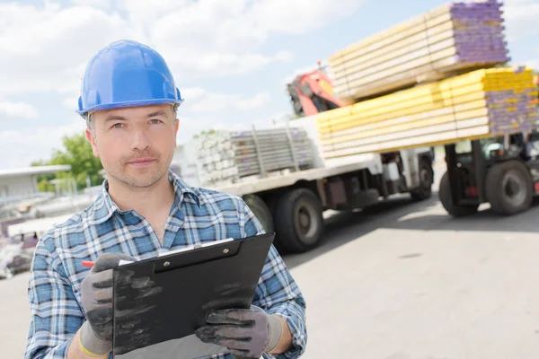 Man with clipboard, forklift unloading lorry in background — Stock Photo, Image