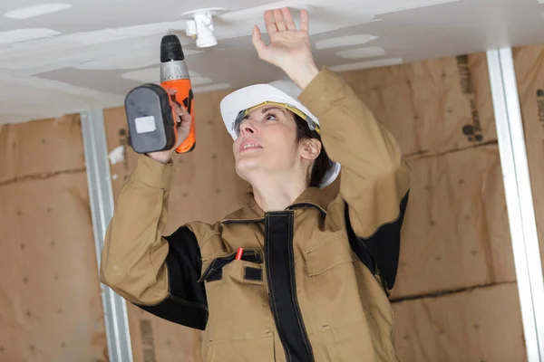 Mooie vrouw met de bouw van perforatie boren van gat in het plafond — Stockfoto