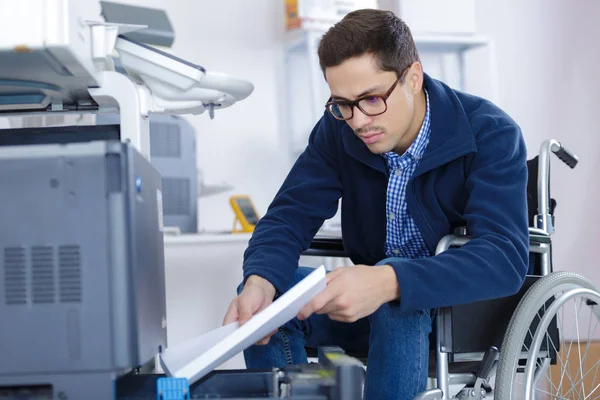 Man in rolstoel zet papier in de papierinvoer van de printer — Stockfoto